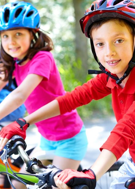 Tre glada barn på varsin cykel med cykelhjälm.